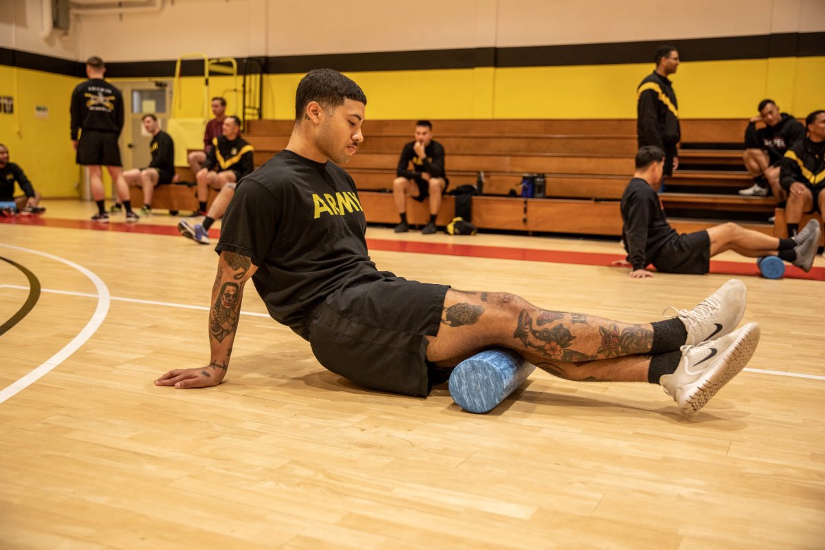 Deportista sentado en una pista pasando un foam roller por el gemelo.