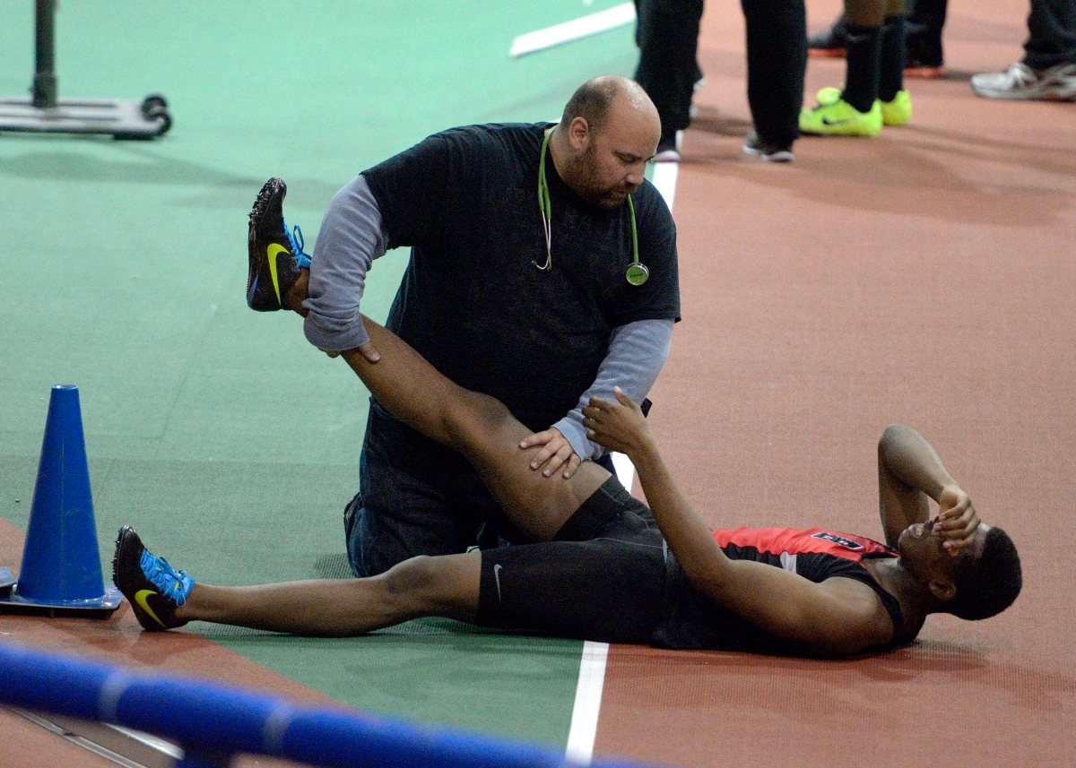 Un atleta tumbado en la pista mientras otra persona le estira la pierna.