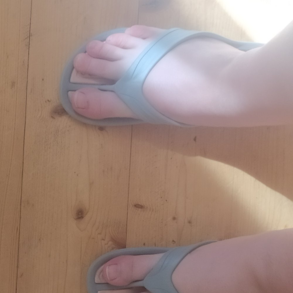 Pies con chanclas sobre un suelo de madera.