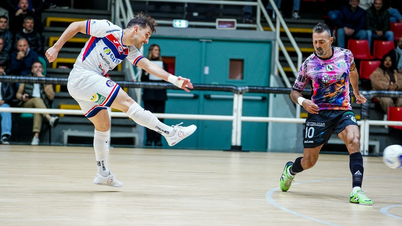 Jugador de fútbol sala chutando en una pista de parquet durante un partido, con un rival defendiendo