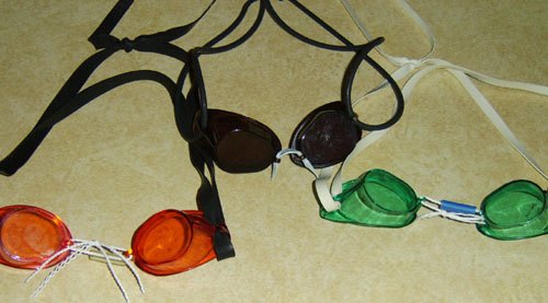 Tres pares de gafas suecas de natación, sin junta, con lentes negras, naranjas y verdes y el puente de la nariz de cordón.